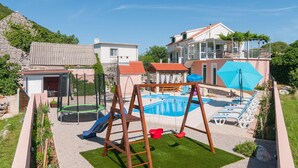 Un jardin avec une piscine, un trampoline, une balançoire et un toboggan.