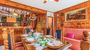 Un coin repas avec une table en bois dressée pour quatre personnes, entourée de chaises en bois. Un canapé rouge est visible au fond.