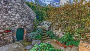 Un bâtiment en pierre avec une porte verte, entouré d’une végétation luxuriante et doté d’un petit escalier menant à un niveau supérieur.