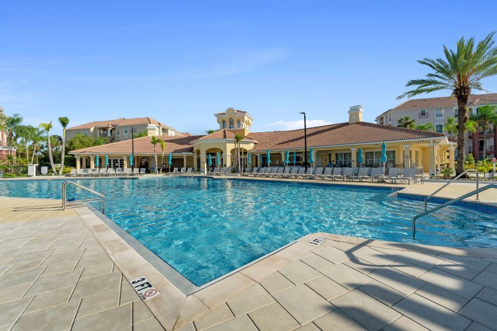 A swimming pool with lounge chairs and umbrellas, surrounded by buildings with a Mediterranean architectural style.