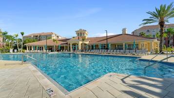 A swimming pool with lounge chairs and umbrellas, surrounded by buildings with a Mediterranean architectural style.