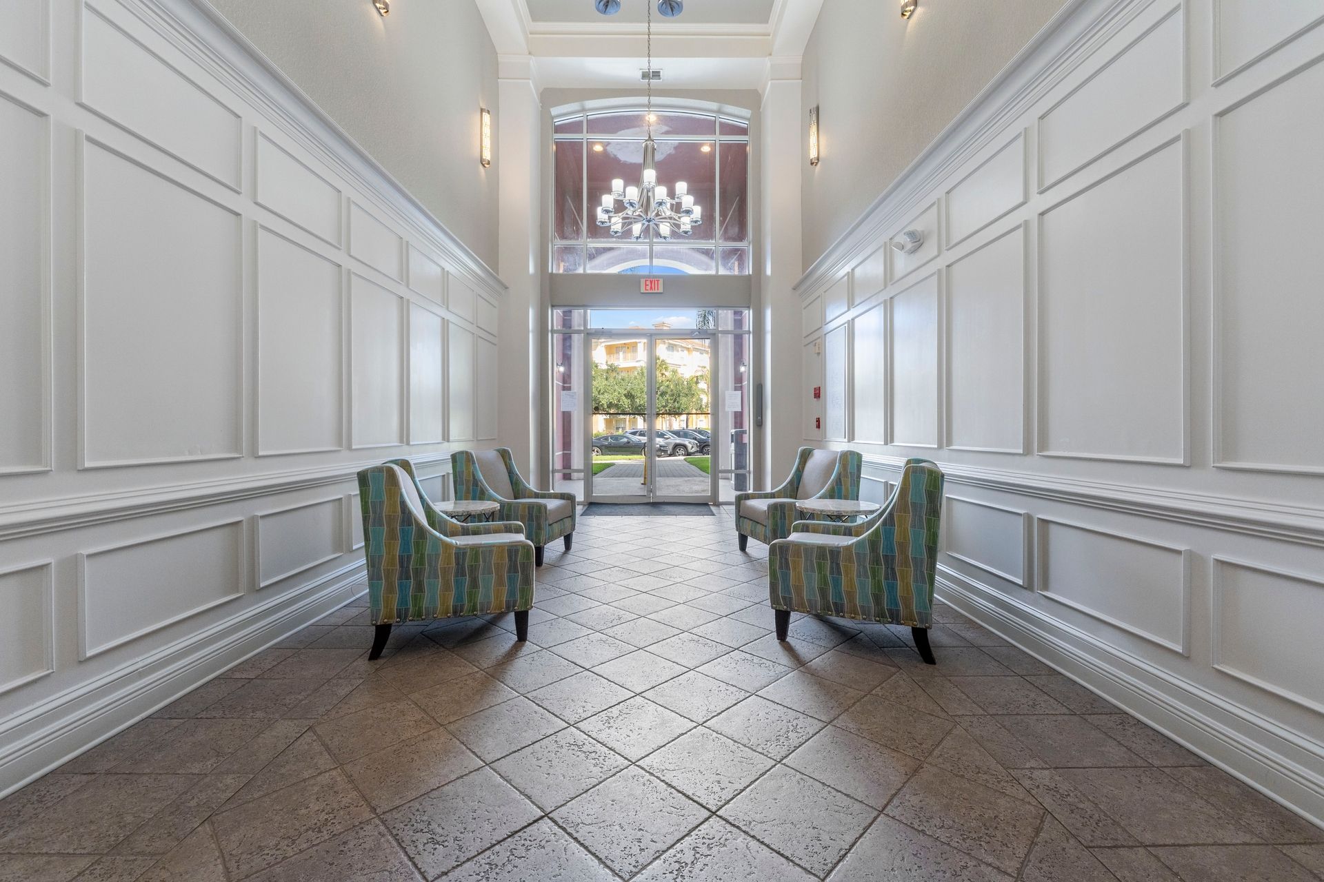 A hotel lobby with a high ceiling, a chandelier, and a view of the outside through a glass door.