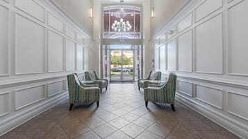 A hotel lobby with a high ceiling, a chandelier, and a view of the outside through a glass door.