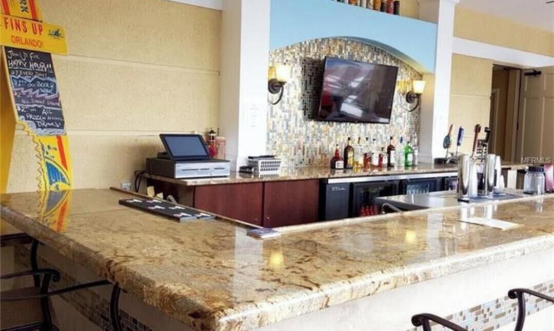 A bar area with a flat-screen TV, a laptop, and a variety of bottles.
