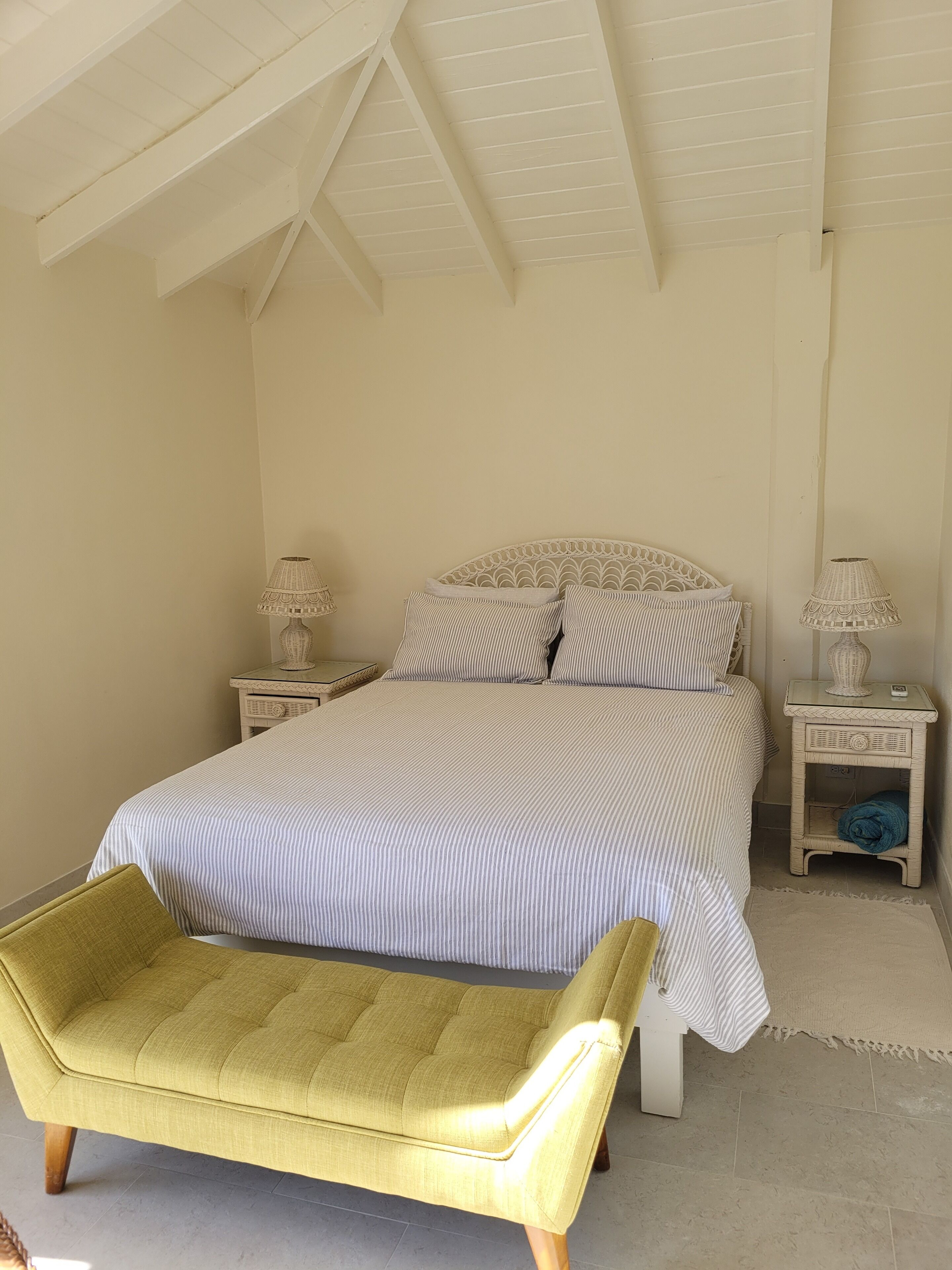 A bedroom with a bed, two bedside tables with lamps, a bench, and a high ceiling with exposed beams.