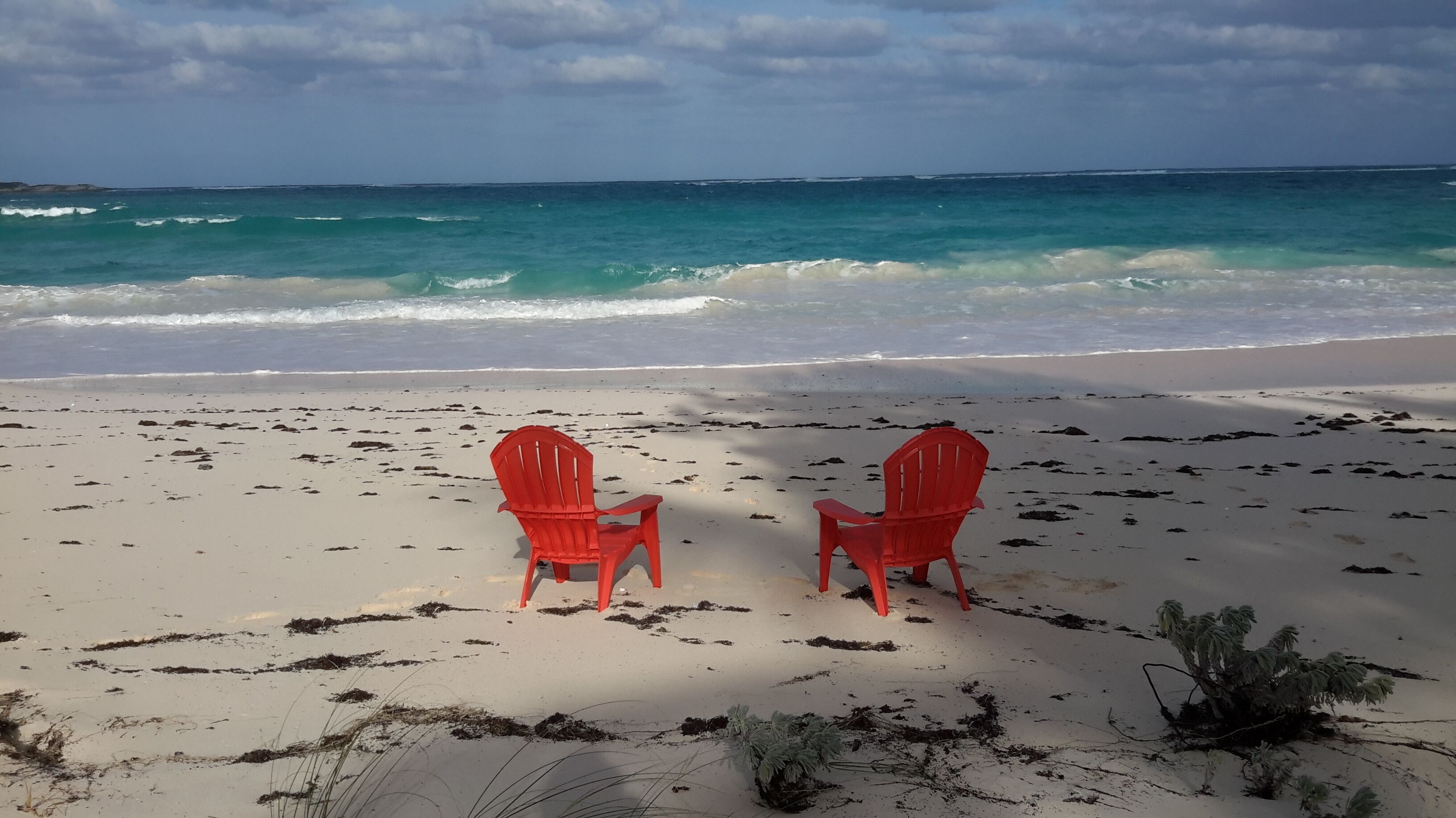 Two red chairs facing the ocean on a sandy beach.