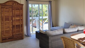 A spacious room with a high ceiling, a large wardrobe, a wicker sofa, and a dining area with a table and chairs.