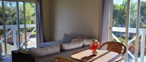 Una habitación soleada con techo alto, un ventanal grande, un sofá, una mesa con sillas y un ventilador de techo.