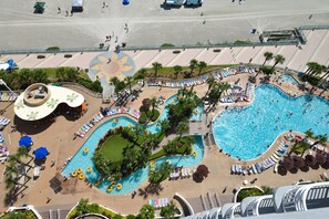 Luchtbeeld van een resort met een groot zwembad, meerdere ligbedden en een kinderspeelplaats.