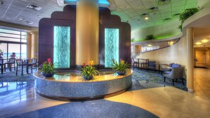 A lobby with a central fountain, seating areas, and a staircase leading to an upper level.