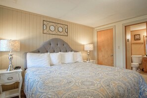 A bedroom with a large bed, two bedside tables with lamps, a wooden door, and a wall-mounted artwork. - Powderidge #14:  2 Bedrooms, 2.5 Bath: Slope Side, Wood Fireplace. (Snowshoe)
