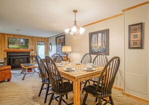 A dining room with a wooden table set for six, surrounded by black chairs. A fireplace is visible in the background, and there are framed pictures on the walls. - Powderidge #14:  2 Bedrooms, 2.5 Bath: Slope Side, Wood Fireplace. (Snowshoe)