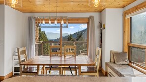 A wooden dining table with chairs, a bench, and a view of mountains through large windows.