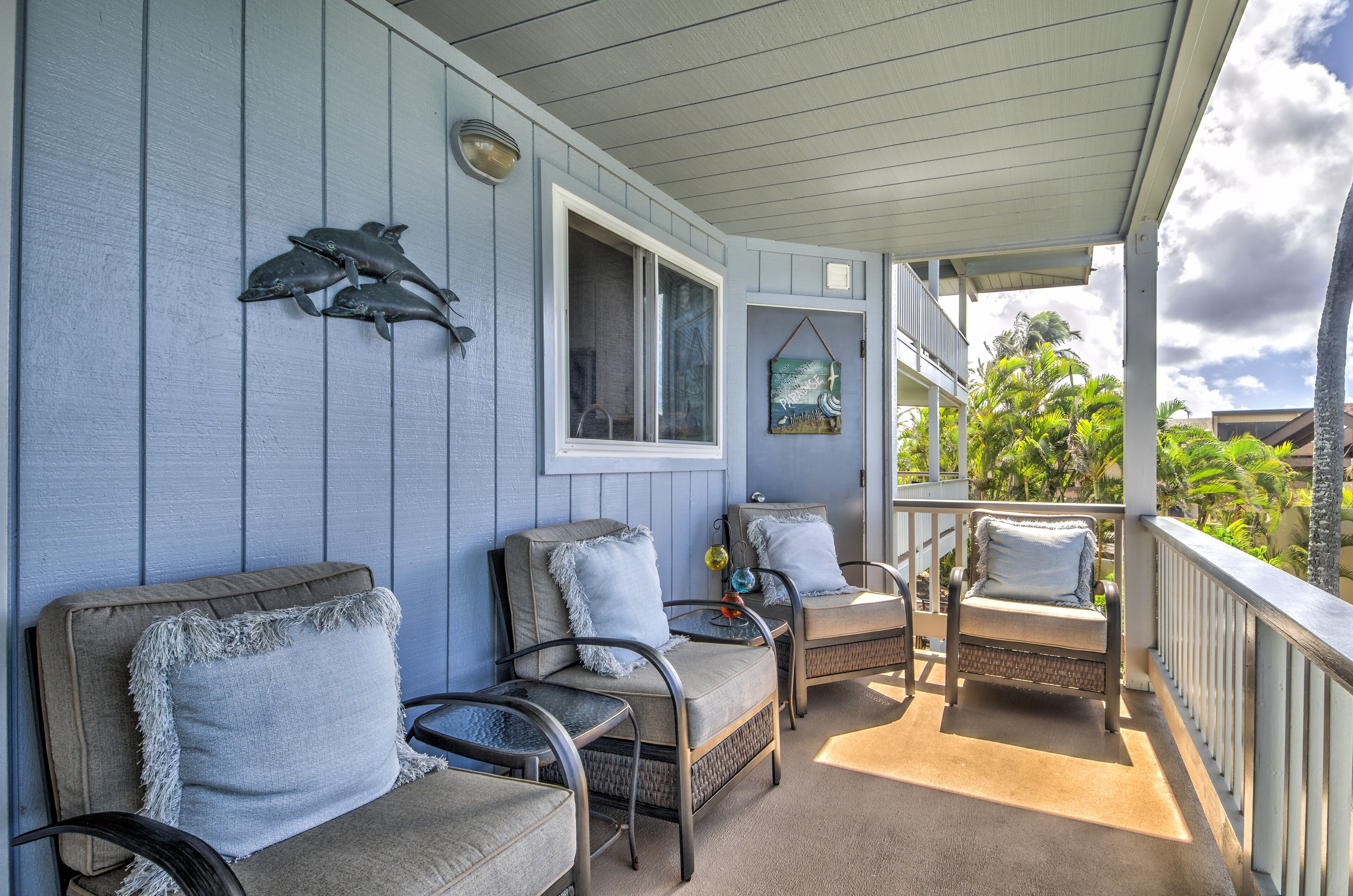 A covered porch with two wicker chairs and a table, a window, and a wall-mounted dolphin sculpture.