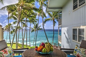 A balcony with a view of the ocean and palm trees, a bowl of fruit, and a white building with windows. - Poipu Palms 202...Oceanfront, Palm Trees and the Beautiful Blue Pacific Ocean! (Poipu)