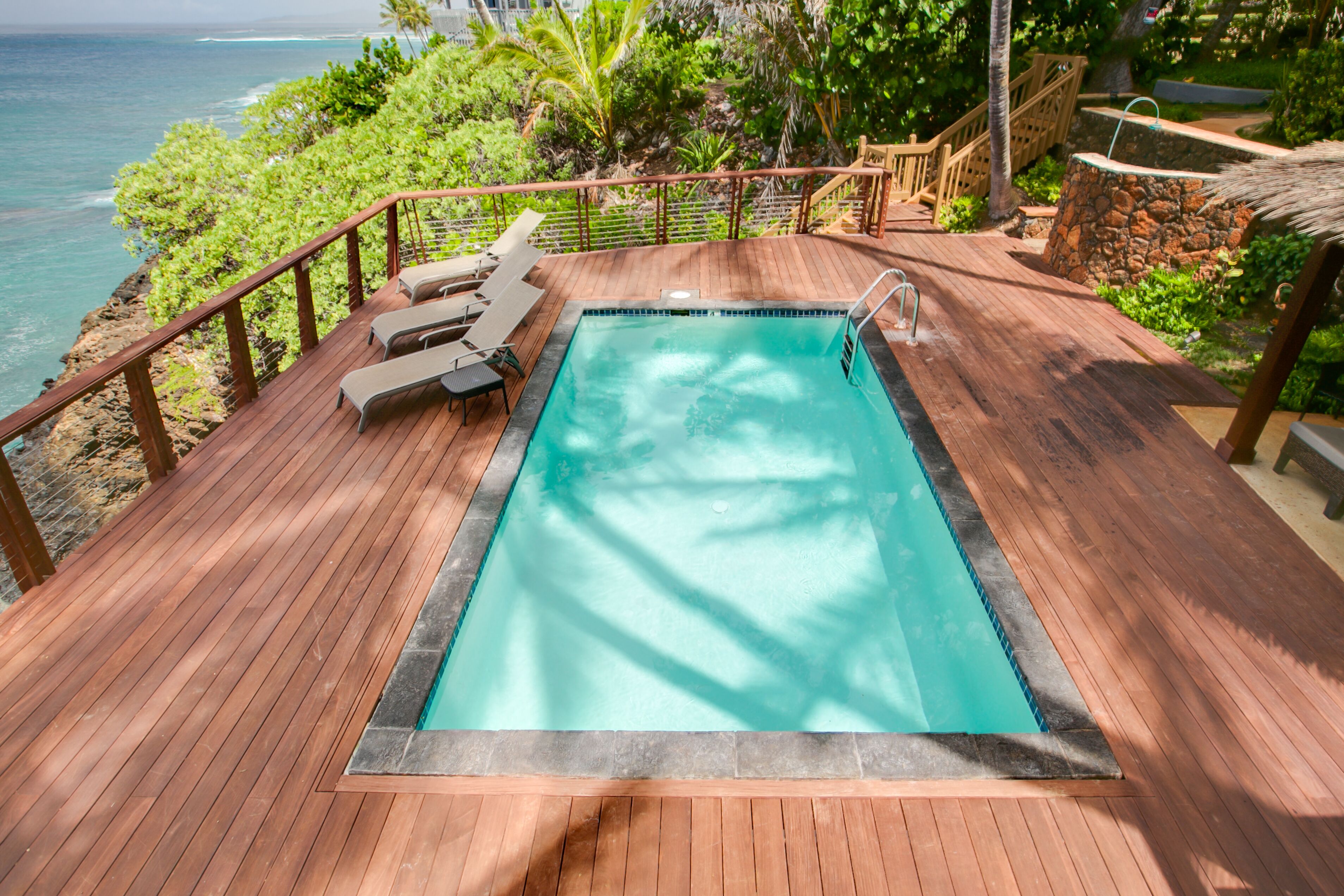 Eine Holzterrasse mit Swimmingpool, Liegestühlen und Blick aufs Meer.