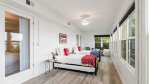 A bedroom with a bed, bedside tables, a ceiling fan, and large windows.