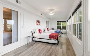 Ein Schlafzimmer mit Bett, Nachttischen, Deckenventilator und großen Fenstern.
