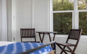 A room with two wooden chairs and a small table, a white door, and a window with a view of greenery. - Lakefront Beach Home + Pet Friendly, Grill & Bikes (Santa Rosa Beach)