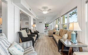A spacious hallway with wicker furniture, a ceiling fan, and large windows.