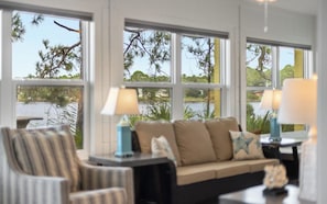 A room with a sofa, two lamps, and a view of a body of water through large windows.