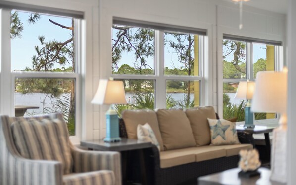 A room with a sofa, two lamps, and a view of a body of water through large windows.