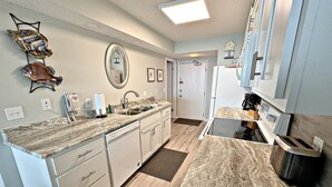 A modern kitchen with a granite countertop, white cabinetry, a built-in oven, and a microwave. - Time to get… 🎶 Knee deep in the water somewhere! 🎶 on island time! (Gulf Shores)