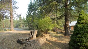 Un chalet rustique entouré d’une forêt dense, avec un mur en pierre et une clôture en bois.
