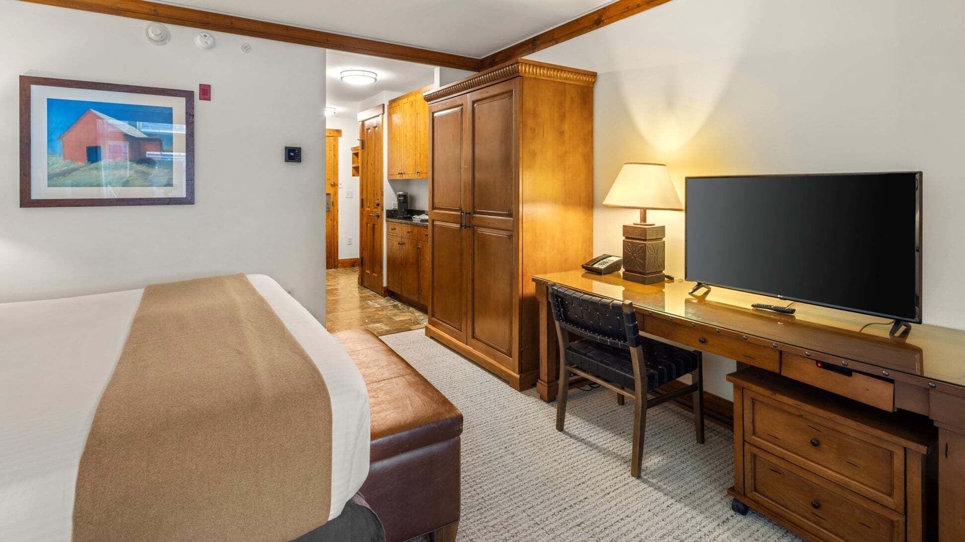 A hotel room with a bed, desk, TV, and wooden wardrobe.