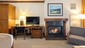 A hotel room with a wooden desk, a television, a fireplace, a sofa, and a painting on the wall.