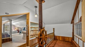 Interior de madera con una gran rueda de madera, un espejo y vistas de una habitación con cama y ventana.