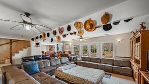 Un salón amplio con un sofá modular grande, un ventilador de techo y una colección de sombreros colgados en la pared.