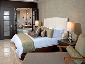 Relax in a spacious room with a large bed, sofa, and armchair, featuring a bedside table and a bathroom with a vanity and shower.
