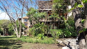 Um edifício de vários andares com varandas, rodeado por vegetação exuberante e árvores.