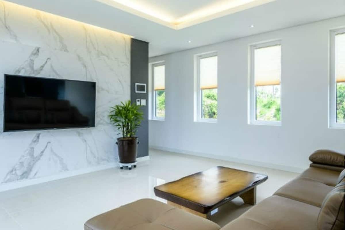 Uma sala de estar moderna com uma televisão de tela plana presa a uma parede de mármore, uma mesa de centro de madeira e um sofá bege.