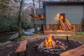 A cabin with a deck, a fire pit, and a river in the background. - A River Runs Thru It | 3BR Riverfront| in Helen (Helen)