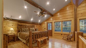 Un dormitorio tipo cabaña de troncos con una cama de madera, un banco, una mecedora y un ventilador de techo.
