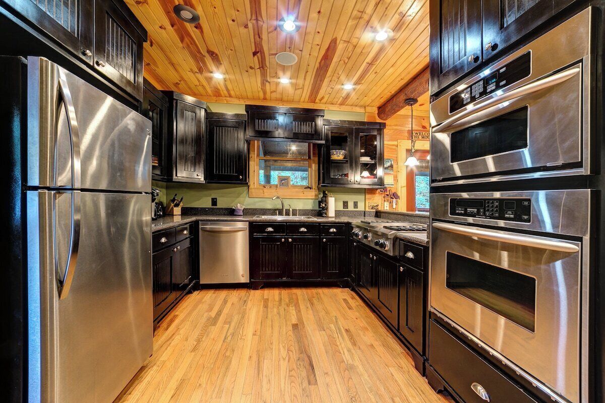 A modern kitchen with stainless steel appliances, wooden flooring, and dark cabinetry.