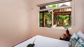 A bedroom with a large window, a bed, a bedside table with a plant, and a view of a garden. - Casa Tropical☙Remodeled Beach Oasis Perfect for resting and relaxing ❧ (Tamarindo)