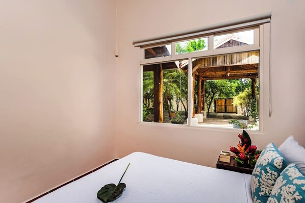 Un dormitorio con un ventanal grande, una cama, una mesita de noche con una planta y vistas a un jardín.