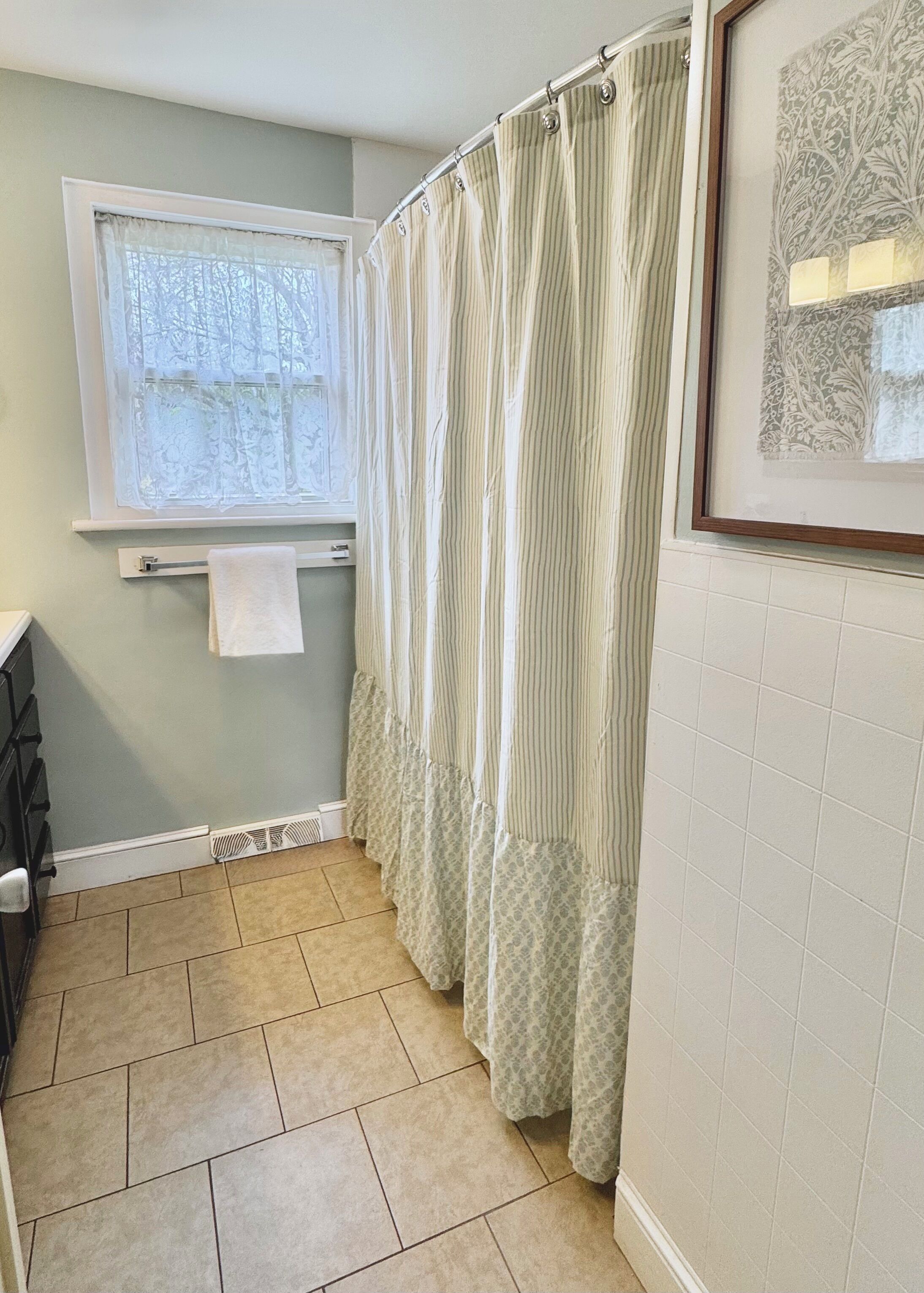 A bathroom with a window, a towel rack, a shower curtain, and a tiled floor.