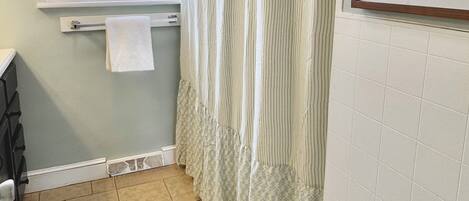A bathroom with a window, a towel rack, a shower curtain, and a tiled floor.