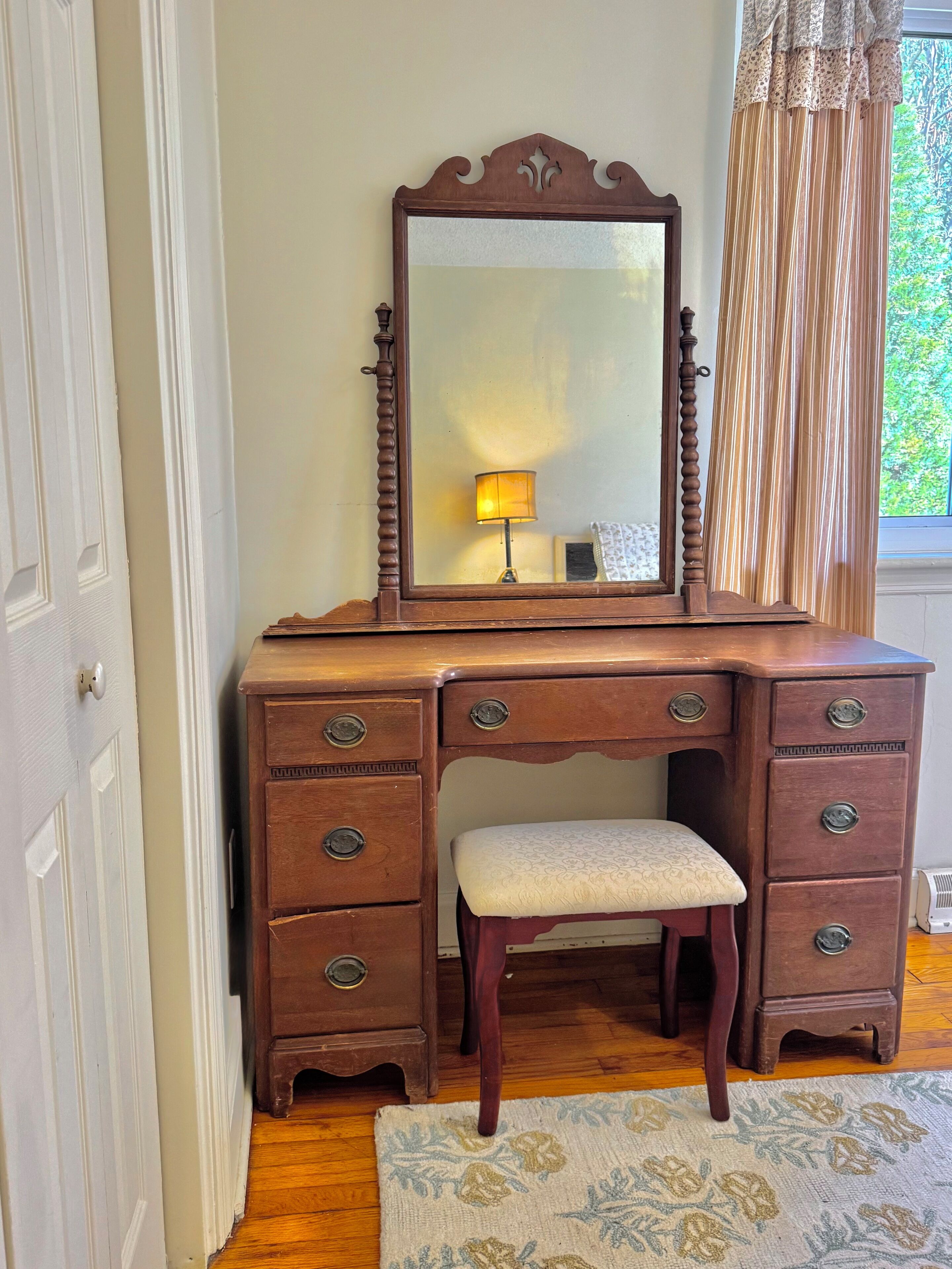 Une commode en bois avec un miroir, des tiroirs et un banc.