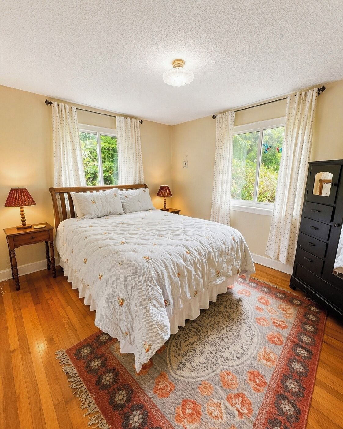 A bedroom with a large bed, two bedside tables, a dresser, and a window with curtains.