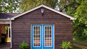 Uma cabana de madeira com porta azul, duas plantas em vasos e o número '188' na lateral.