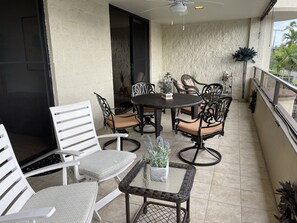 A covered outdoor patio with a round table and chairs, a white chair, and potted plants. - Fabulous Ocean Views : Whales : Dolphins : Big Island Fun! (Kailua-Kona)