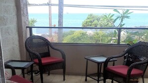 Un balcón con mobiliario de mimbre, incluyendo sillas y una mesita, y vistas al mar.
