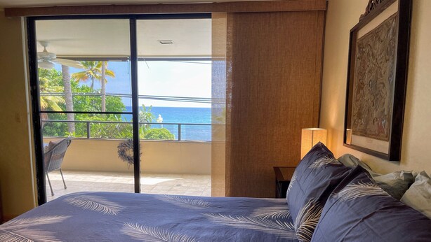 Un dormitorio con cama, un balcón con vista al océano y un cuadro en la pared.