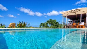 A clear blue pool with a lounge area featuring striped chairs and a covered seating area.
