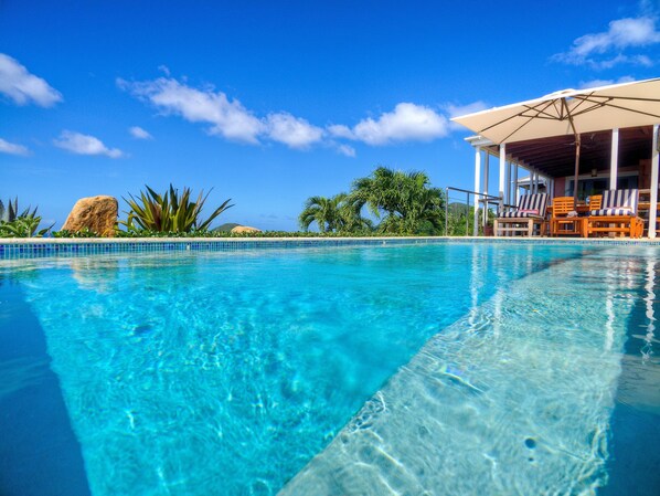 Une piscine d’un bleu éclatant, avec un espace de détente comprenant des chaises à rayures et un coin salon abrité.